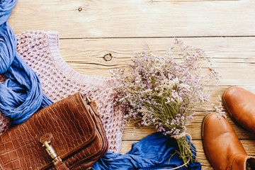 Red shoes, purple bouquet, sweater, scarf and leather bag on a vintage wooden background, concept