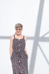 Portrait of a happy fashionable woman in stylish clothes in a light room on a white background with shadows. Smiling stylish woman with short hair poses against the backdrop of a white abstract wall.