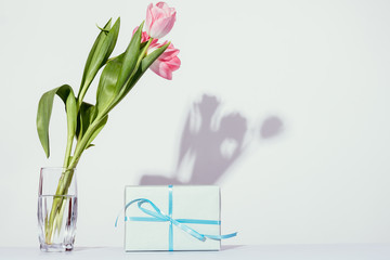 Pink tulips bouquet in glass vase next to gift box