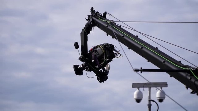 Broadcast TV camera on a moving jimmy jib crane arm, next to surveillance cctv cameras at a outdoor event
(slow motion)