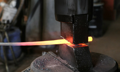 Using pneumatic hammer to shape hot metal. Making the sword out of metal. Side view.