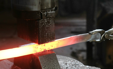 Using pneumatic hammer to shape hot metal. Making the sword out of metal. Side view.