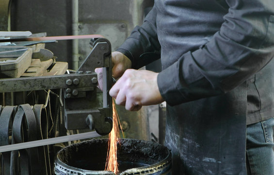 Grinding billets of metal on a belt-grinding machine. Close-up of a man's hand.