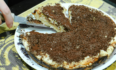 Closeup of a woman's hand cut a piece off a homemade cake with chocolate chips and put it on a plate.