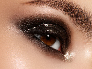 Close up of blue woman eye with beautiful brown with shades smokey eyes makeup. Modern fashion make...