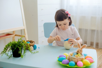 child paints eggs on wooden workpiece eggs sitting at table in a white room