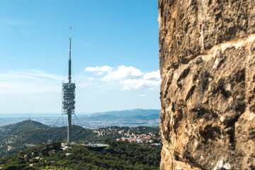 Obraz premium Aerial (panoramic or cityscape) view of the green forest hills of Barcelona (Catalonia, Spain) and TV tower Torre de Collserola from the highest point of Tibidabo Torre de Collserola