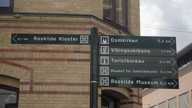 Signs pointing towards famous attractions in Roskilde, Denmark in slow motion with upwards movement at the end
