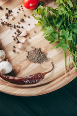 Spices: chili, black pepper, garlic, cumin, coriander, sweet pepper lie on a brown round wooden board on a black table. Place under the text.