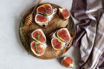Mini bruschetta (toast or sandwich) with ricotta (cream cheese), fig, honey and thyme served on wooden rustic plate. Healthy food concept. 