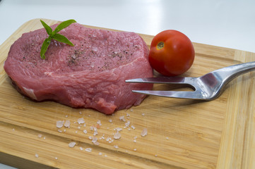 raw beef steak on cutting board with cherry tomatoes and basil leaf