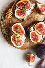 Mini bruschetta (toast or sandwich) with ricotta (cream cheese), fig, honey and thyme served on wooden rustic plate. Healthy food concept. 