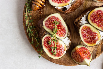 Mini bruschetta (toast or sandwich) with ricotta (cream cheese), fig, honey and thyme served on wooden rustic plate. Healthy food concept. 