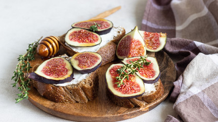 Mini bruschetta (toast or sandwich) with ricotta (cream cheese), fig, honey and thyme served on wooden rustic plate. Healthy food concept. 