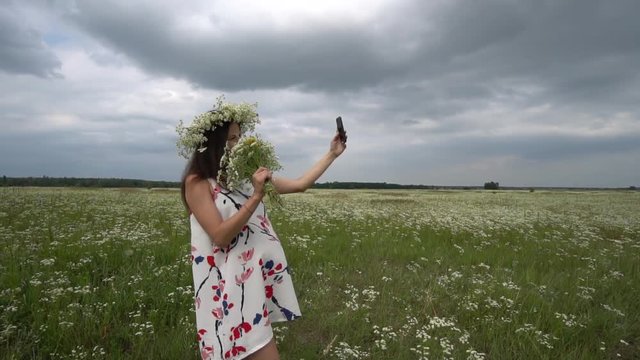 Beautiful pregnant girl doing selfie, photo with camomile flowers outside.