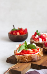 Italian bruschetta with chopped cherry tomatoes, mozzarella cheese and basil on wooden cutting board. 