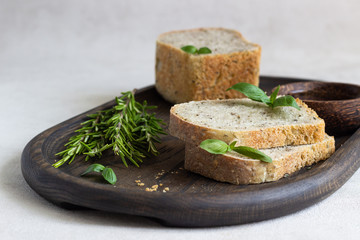 Loaf of fresh baked rye bread with rosemary, basil and olive oil over dark wooden tray. 