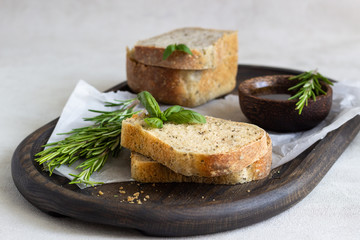 Loaf of fresh baked rye bread with rosemary, basil and olive oil over dark wooden tray. 