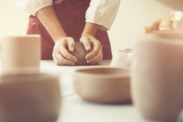 woman porter shaping ball of clay and unbacked handmade crockery on the table ready to be put in...
