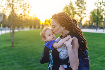 Young happy mom with baby son in ergo backpack walking in the Park. Concept of modern parents