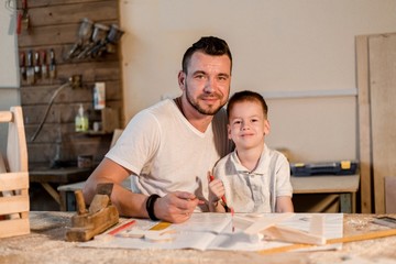 Father and son in the workshop playing are designing a model of the future wooden toys