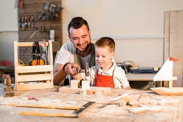Dad and son hammer together a nail standing in the carpenter's shop making wooden figurines