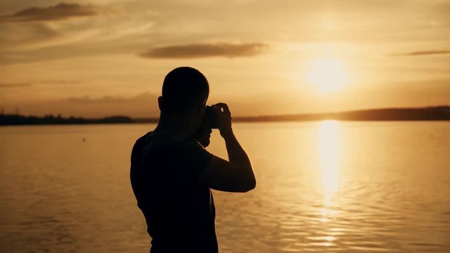 Silhouette of photographer taking photos in the river at sunset time.