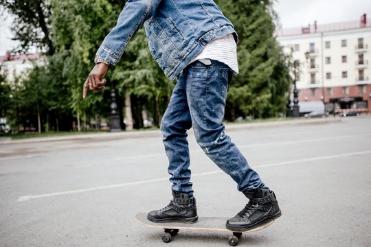 African man in denim jacket skateboarding in the street