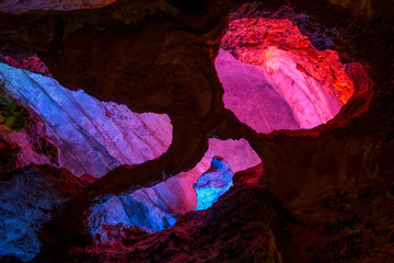Abstract cave interior chamber photograph - colored lights, bumpy rock surfaces and exotic rock formations. Textures, rugged surface, underground exploration. Alien planet concept, cave geology.