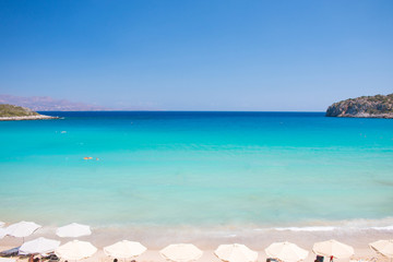 Fototapeta premium Beautiful colorful beach at Crete island, Greece. Voulisma paradise beach with umbrella and sunbeds. Summer vacation travel holiday background concept.
