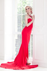 Elegant woman with perfect makeup and red long dress, posing near window. indoor, Studio shot