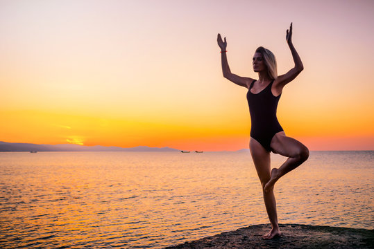 Beautiful girl in black doing yoga on the pier by the sea, standing asana Vrikshasana at sunrise. Healthy lifestyle. © indigo_nifght