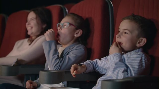 Children watching movie enthusiastically in cinema. Happy boy and girl watching comedy film at cinema. Girl coughing in cinema. Young spectators enjoy fun cartoon. Child entertainment concept