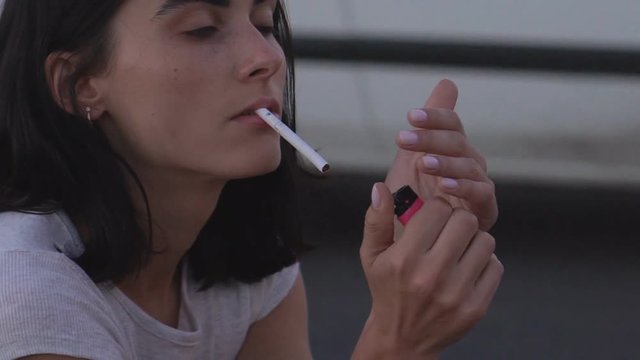 young grump brunette lit a cigarette. A woman is sitting on the side of the motorway. HD slowmotion