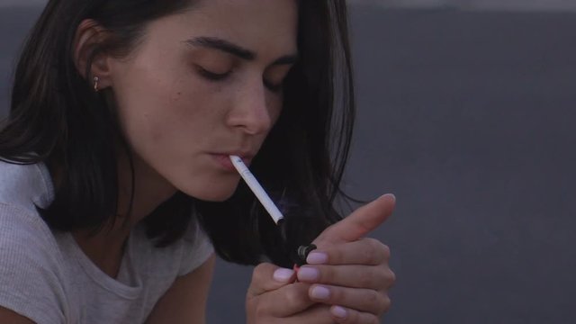 young grump brunette lit a cigarette. A woman is sitting on the side of the motorway. HD slowmotion