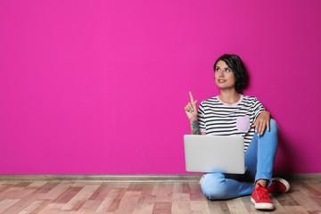 Young woman with modern laptop sitting on floor near color wall