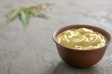 Bowl with hemp lotion and space for text on grey background