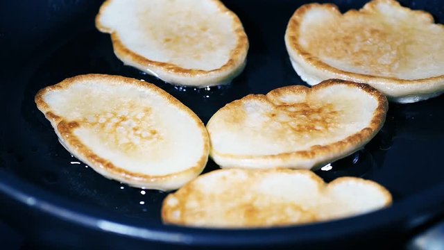Grilling small pancakes in a frying pan. Bubbles on the surface of a pancake