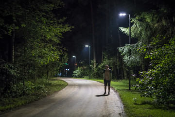 alone young man in casual walking on the night forest road with the street lights