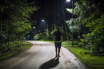 alone young man in casual walking on the night forest road with the street lights