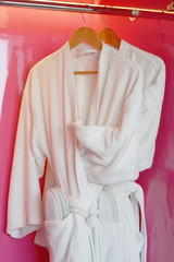Two white coats hanging on the door. Hotel dressing gowns on the door hanger.