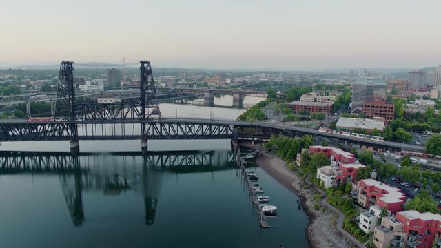 Drone aerial reveal of 2 trolley's crossing the Steel Bridge with flyover of Broadway Bridge and downtown Portland at sunrise in the summer