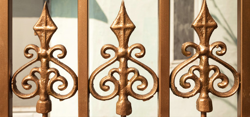 Golden wrought fence detail close-up background. Forged ornate beautiful pattern golden  gate