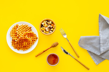 Hot round waffles ready to eat. Belgian recipe. Waffles on plate near honey and dried fruits on yellow background top view copy space