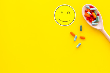 Fototapeta premium Reception of medicines concept. Recovery. Pills in spoon near smile face emoji on yellow background top view copy space