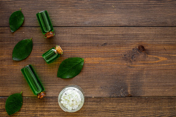 Natural hipoallergenic cosmetics with tea tree essential oil. Oil, lotion, leaves on dark wooden background top view copy space