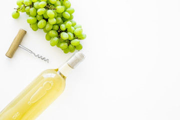 Open the wine concept. White wine in glass bottle near bunch of grapes and corkscrew on white background top view copy space