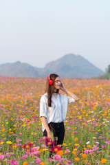 Pretty fashion cool girl listening to music in red headphones in the field of flowers.