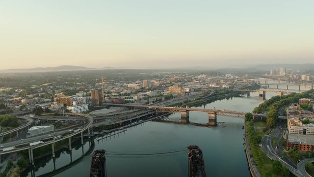 Drone aerial sunrise of the Steel Bridge with a trolley and 2 buses crossing it and 4 other bridges in downtown Portland on a summer morning