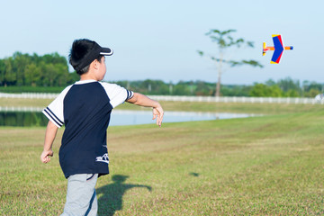 Happy asian kid playing with toy airplane against green yard background. Boy throw foam plane in green field.  